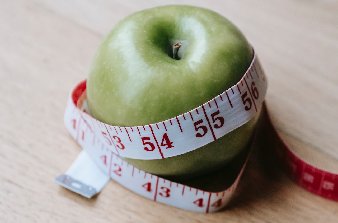 soczyste jabłko otoczone miarą krawiecką nawiązujące do funkcjonowania układu pokarmowego i przyspieszania metabolizmu